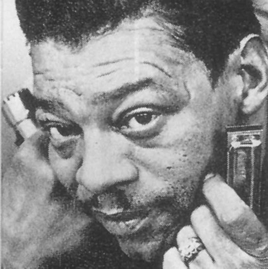 Little Walter in an extreme closeup of his phase. He wears a blingy ring and holds a harmonica in each hand near his face