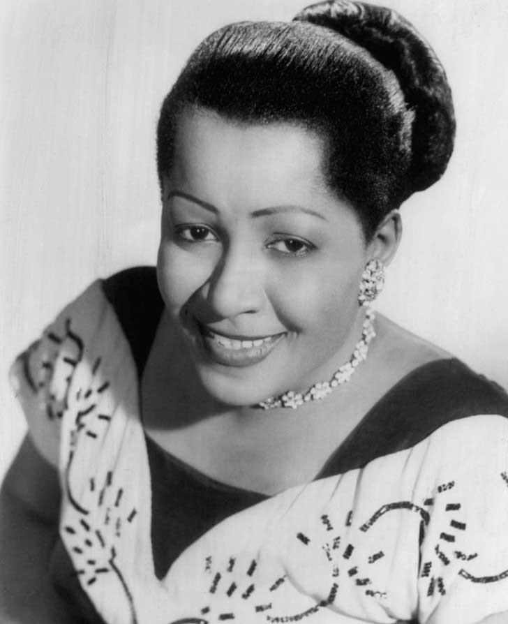 A portrait of a smiling Nellie Lutcher in a dress with a swirling design, pearls and hair in a bun