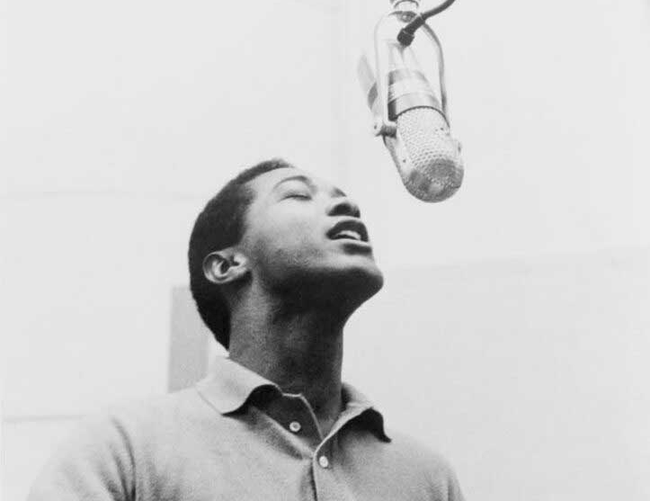 Sam Cooke croons into a microphone hanging above him; his eyes are closed and he wears a light-colored collared sweater