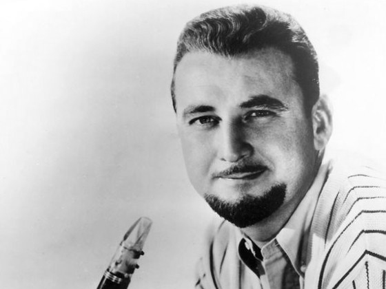 Pete lays on his stomach, propped up and holding his clarinet. he wears a white-striped shirt