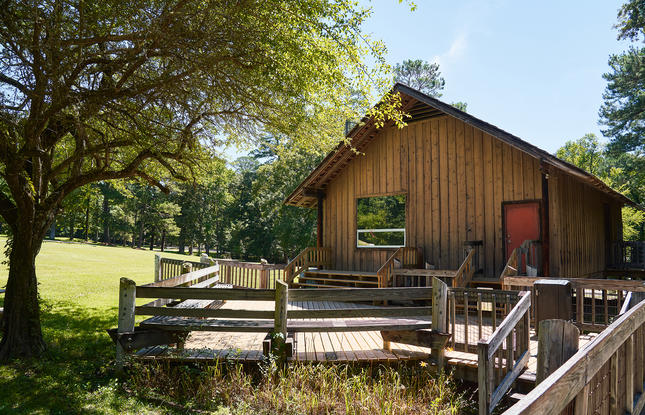 A wooden building at Los Adaes State Historic Site on a sunny day with a tree next to it