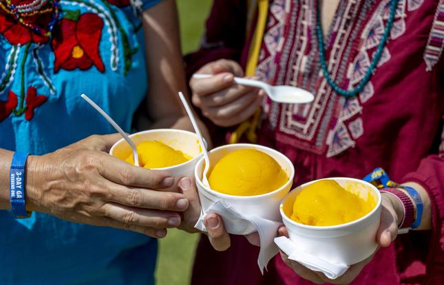 Hands hold three bright orange mango freezes at the New Orleans Jazz &amp; Heritage Festival.