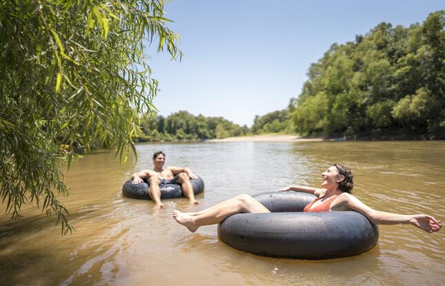 A man and a woman relax on black inner tubes on a muddy river in Louisiana.