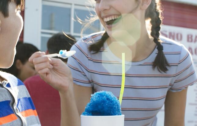 A teenage girl laughs while taking a bite from a bright blue snoball.