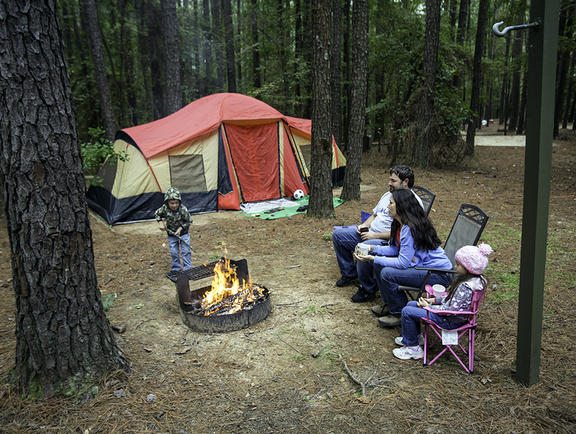 A family’s campsite at Lake D'Arbonne State Park, featuring several chairs, a roaring fire and their tent in the background.