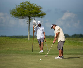 A man in a neon green golf polo takes a swing out of a sand trap at Wetlands Golf Course.