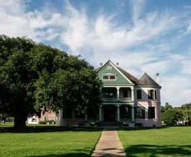 Southdown Plantation, a green and pink building, is partially shaded by a large green tree.