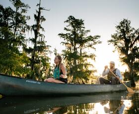 Two people canoeing on Lake Martin at sunset with cypress trees reflected in the water.