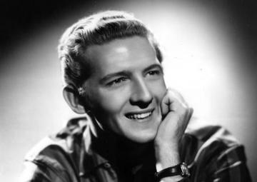 Under a spotlight, Jerry poses for a portrait. He wears a striped shirt and rests his chin on one arm.